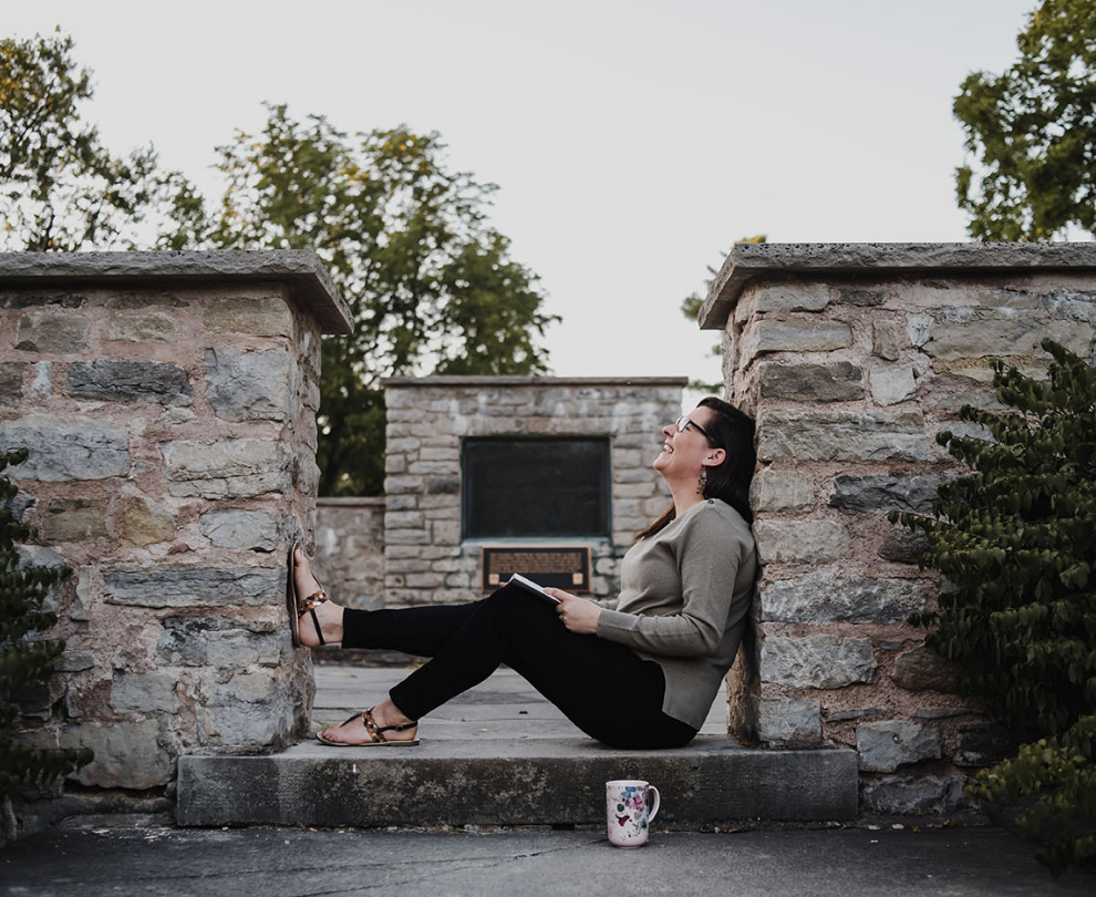 Jess leaning against a wall with notebook